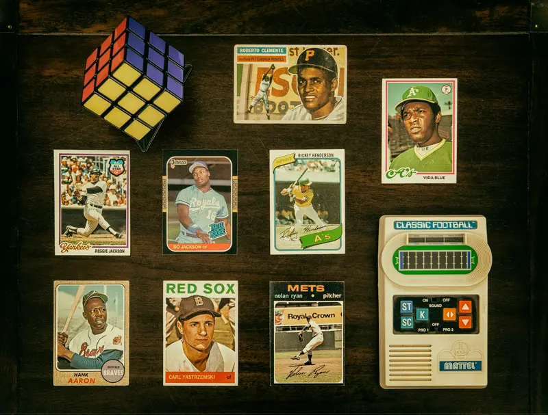 Vintage baseball cards laid out on a dark table beside a Rubik's cube and a handheld game